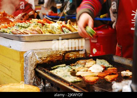 Night food market in South Korea, Seoul with woman cooking on grill. Stock Photo