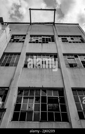 A vertical low angle grayscale shot of an old abandoned building with broken windows on a cloudy day Stock Photo