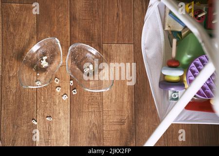 The plate fell on the wooden floor and broke against the background of children's toys. The concept of accidents in the kitchen is dangerous for young children in the house. High quality photo Stock Photo