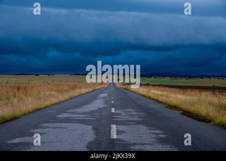 A long road through the fields in the countryside under the cloudy sky in the evening Stock Photo