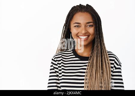 Close up portrait of smiling black girl looking relaxed and happy, standing in striped blouse against white background Stock Photo