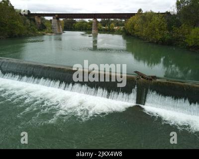 A view of a dam on a river flowing through its banks covered with greenery Stock Photo