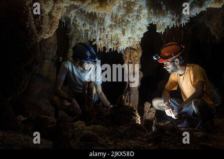 The two Hispanic males sitting in front of a light inside the cave Stock Photo