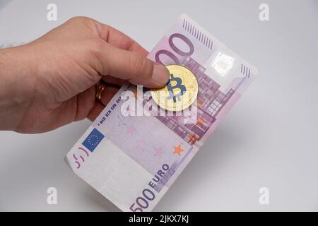 Male hand holding money. Gold bitcoin and 500 euros bank note. Gold BTC coin of cryptocurrency and one five hundred euros banknote holding on men's fi Stock Photo