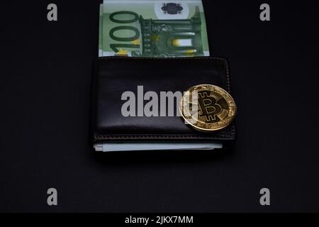 Bitcoin coin on top of wallet with  100 Euros banknotes on a dark background. Golden bitcoin on wallet. Cryptocurrenct, bitcoin and Euro banknote Stock Photo