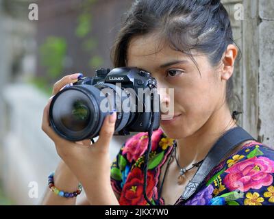 Young attractive female professional Mexican photographer holds DSLR camera Lumix GH5 with both hands and takes photo. Stock Photo