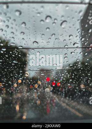 A vertical shot of raindrops on a car window with bokeh lights Stock Photo