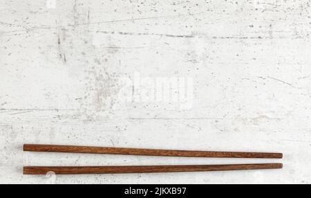 Flat lay photo - pair of dark wood chopsticks on white board. Wide banner for Asian or Chinese food, space for text above Stock Photo