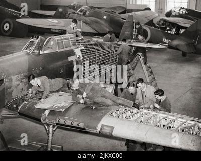Trainee airframe fitters are taught repair procedures on Hawker Hurricane instructional airframe, 1359M, in a hangar at No. 2 School of Technical Training, Cosford, Shropshire, England. The Hurricane flew with No. 111 Squadron RAF before crashing during a forced landing in January 1939. More instructional airframes, including Bristol Blenheim Mark Is and a Fairey Battle, can be seen in the background. Stock Photo