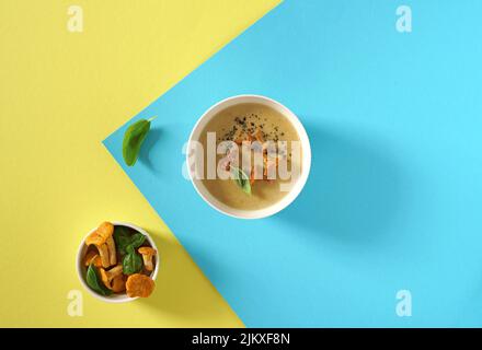 cream soup with mushrooms chanterelles and herbs on a blue and yellow background, top view Stock Photo