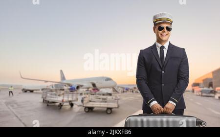 Pilot carrying a suitcase and posing on an airport apron with planes parked in the back Stock Photo