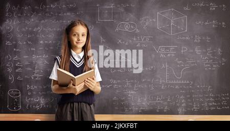 Female pupil with a book standing in front of a blackboard with geometry and math formulas Stock Photo