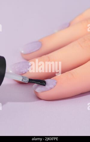 Womans hand with fashionable lavender manicure on pink background