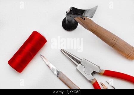 A closeup of the tools isolated on white background. The hammer, circlip pliers, knife, red thread. Stock Photo