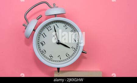 Selective focus on a white alarm clock on a pink background. A fallen white alarm clock showing how time cannot be wasted. Stock Photo