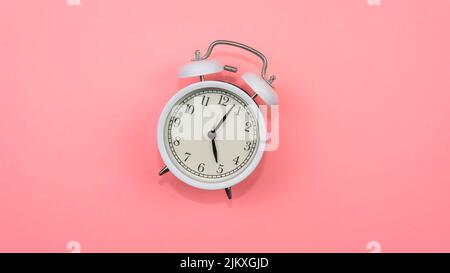Selective focus on a white alarm clock on a pink background. A fallen white alarm clock showing how time cannot be wasted. Stock Photo