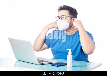 young man wearing mask and taking corona precaution when using laptop on a desk Stock Photo