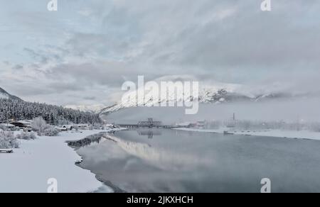 Village of Carcross, Yukon in January with ice fog over Bennett Lake and relections on Nares River Stock Photo