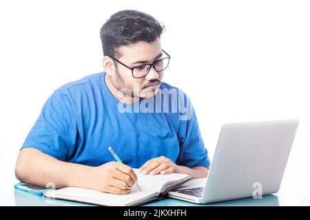 student writing on a notebook or diary while looking at laptop screen Stock Photo
