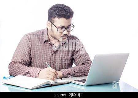 business man writing on diary notepad with pencil looking at laptop screen Stock Photo