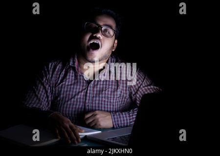 young business man feeling exhausted and yawning at mid night while working on laptop Stock Photo