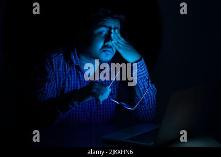 young man relaxing his eyes after using laptop at mid night Stock Photo