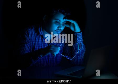 young man with dark circle under eyes working on laptop at late night removed eyeglass Stock Photo