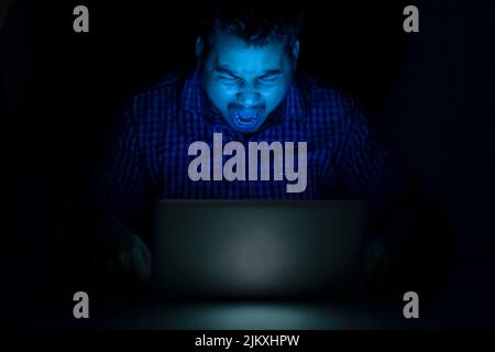 hacker yelling or screaming against the laptop screen at night time Stock Photo