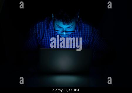 young man typing on laptop keyboard at night and looking over the eyeglass Stock Photo