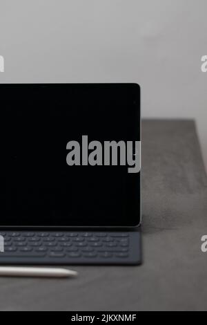 A vertical closeup of a black tablet with a portable keyboard and a white pen on the gray fabric Stock Photo