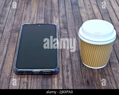 horizontal view of a take away coffee cup with a mobile phone on a wooden table Stock Photo