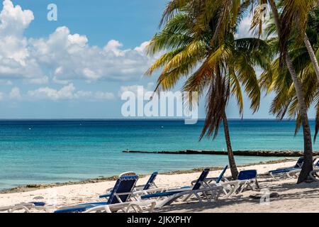 Photo of a Caribbean beach with calm clear blue waters, there is some lapiez  at the shore, and there are a few plastic beach loungers on the white sa Stock Photo