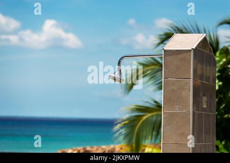 Photo of a metallic shower device in the open air, drops of clear water are falling down from it, you can see the ocean in a blur in the background, a Stock Photo