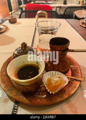 A closeup of a cup of coffee and a glass of water with ancient dishes and a sweet on a tray Stock Photo