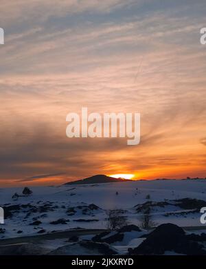A beautiful view of the sunset over a snowy land under a cloudy sky Stock Photo
