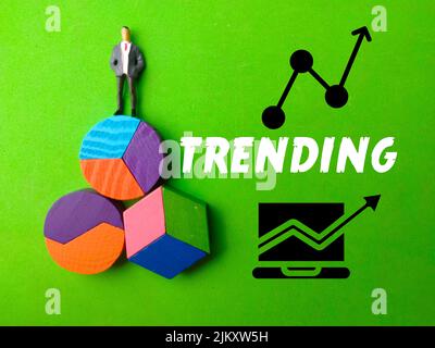 Miniature people,colored block and icon with text TRENDING on green background. Stock Photo