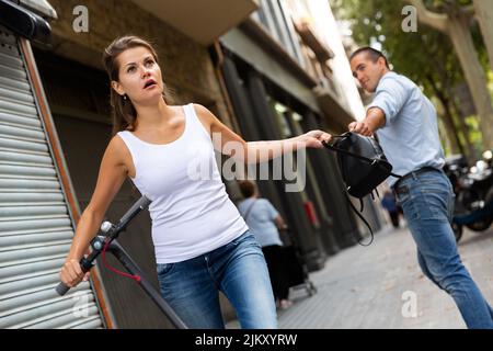 Robbery pulling backpack from woman with scooter Stock Photo