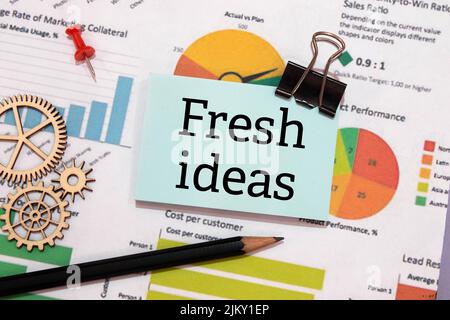 Flower in a pot, calculator, white alarm clock, multi-colored pieces of paper and a white notebook with the text FRESH IDEAS on the desktop. Stock Photo