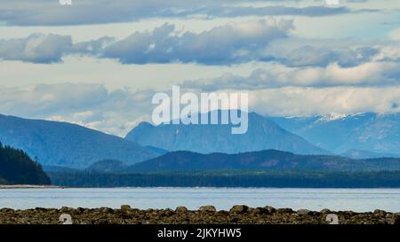 View from a rocky beach of the majestic mountains across the ocean strait on a slightly overcast day Stock Photo