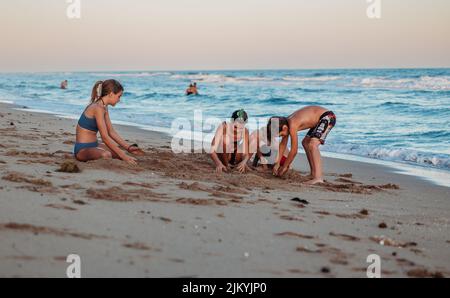 Kids playing and surfing in on the  beach in small waves. Grandmothers watching the kids play. Kids playing on a raft in the waves. Kids catching wave Stock Photo