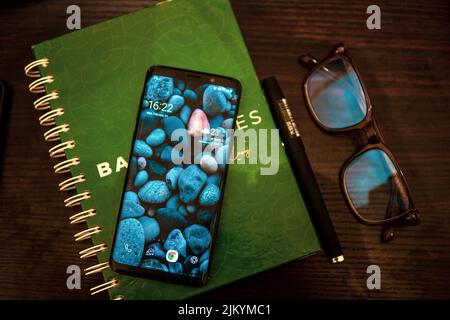 A top shot of a Samsung s9 and eyeglasses on a green notebook on a brown table in an office in Nairobi, Kenya Stock Photo