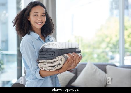 Neatly folded clean laundry is so satisfying. a young woman holding a pile of clean folded laundry. Stock Photo