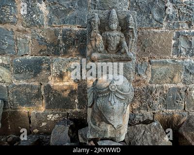 Stock photo of ruined ancient sculpture of Hindu trinity god sitting on elephant, idol carved out off gary color granite sunlight falling on idol, Pic Stock Photo