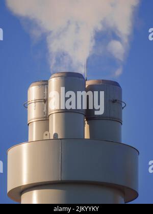 Huge smoke against a blue sky coming out of a factory pipe on a sunny day Stock Photo