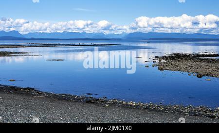 Ocean view from a rocky beach of the beautiful, calm deep blue water and the distant fluffy clouds on a bright summer day. Stock Photo