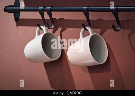 A closeup of white mugs hanging on a brown wall Stock Photo