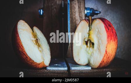 A closeup of a fresh red apple cut in half on a steel cutting machine Stock Photo