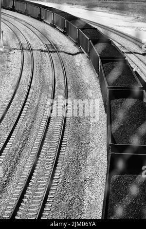 a vertical grayscale shot of train with coal on railway Stock Photo