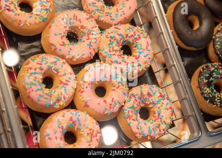 A closeup of sweet donuts on the shelf at a pastry store with pink topping and colorful sparkles Stock Photo