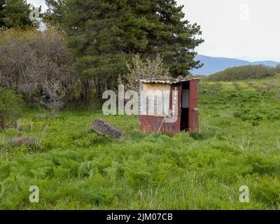 Abandoned small hut on grassland in the countryside in the mountains with many trees Stock Photo